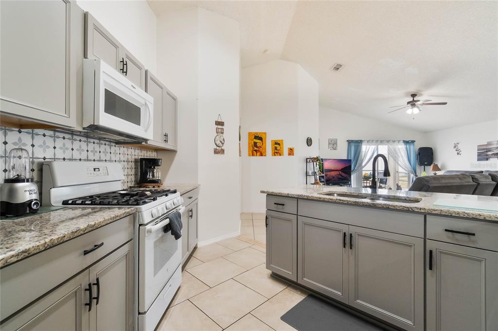 A kitchen with gray cabinets, granite countertops, and a white stove opens to a living area — 640 LADY DIANA DRIVE, DAVENPORT, FL