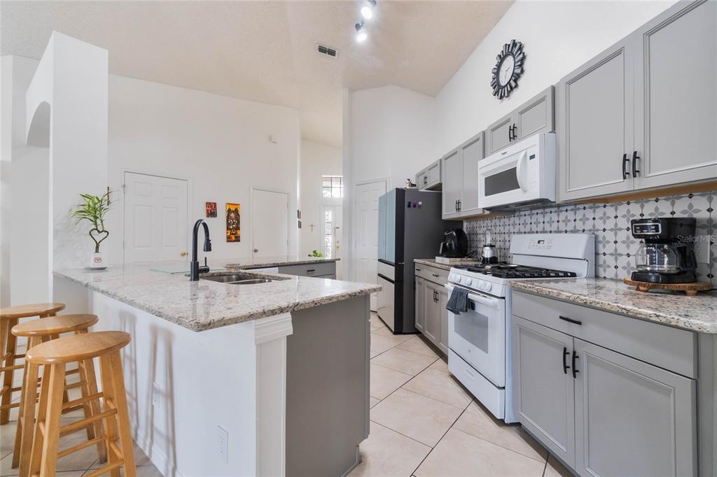 A kitchen features gray cabinets, granite countertops, a white stove, and a breakfast bar — 640 LADY DIANA DRIVE, DAVENPORT, FL