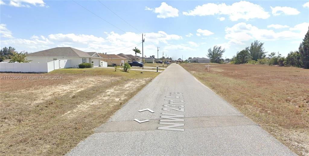 A paved road runs between a residential house and an undeveloped grassy lot — 1926 NW 23RD AVE AVENUE NW, CAPE CORAL, FL
