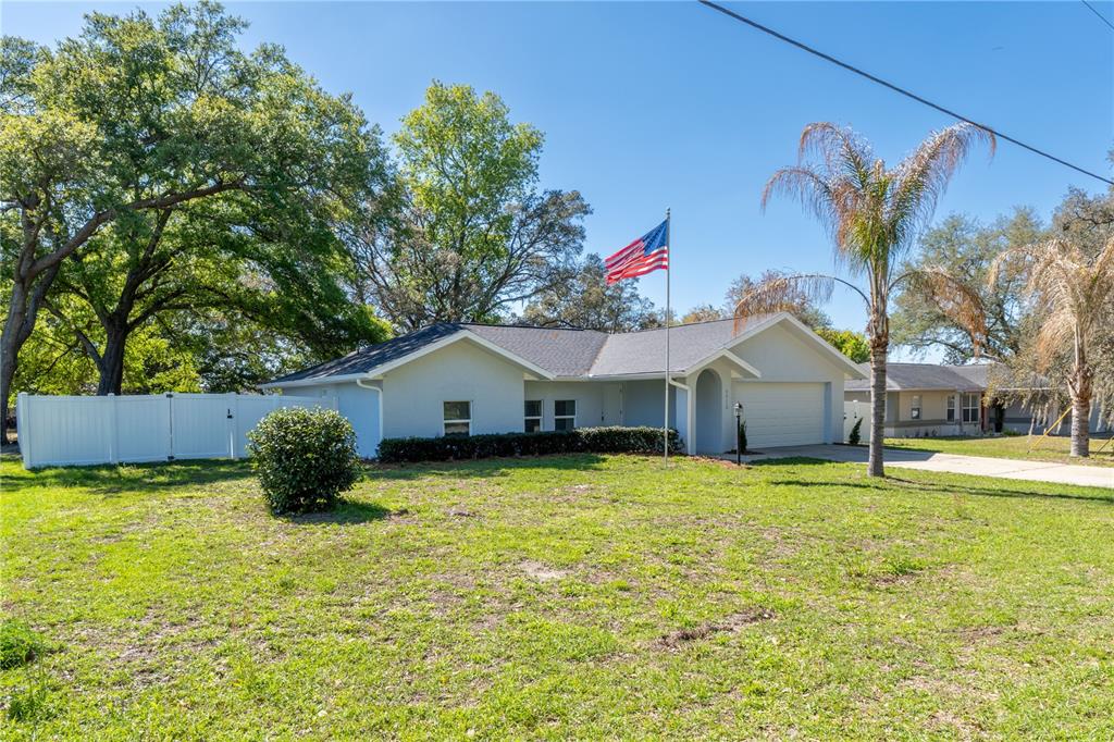 A single-story house with a white exterior, a two-car garage, and an American flag — 5912 SW 111TH PLACE ROAD, OCALA, FL