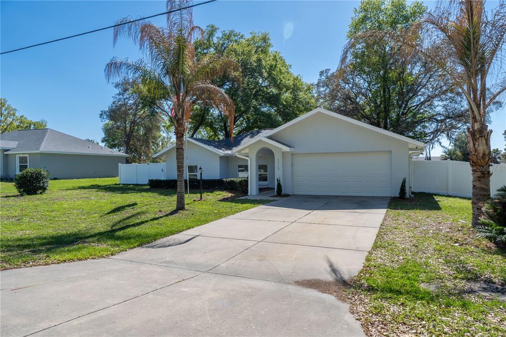 A single-story house with a white garage, concrete driveway, and two palm trees in front — 5912 SW 111TH PLACE ROAD, OCALA, FL