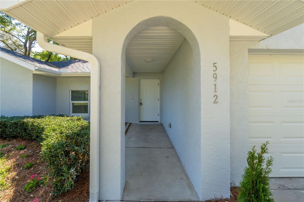 A white house exterior features an arched entryway leading to a front door — 5912 SW 111TH PLACE ROAD, OCALA, FL