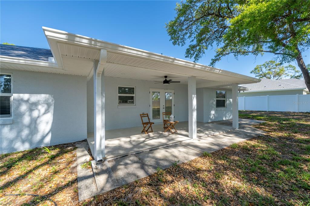 A covered concrete patio features a ceiling fan, two chairs, and white exterior walls — 5912 SW 111TH PLACE ROAD, OCALA, FL