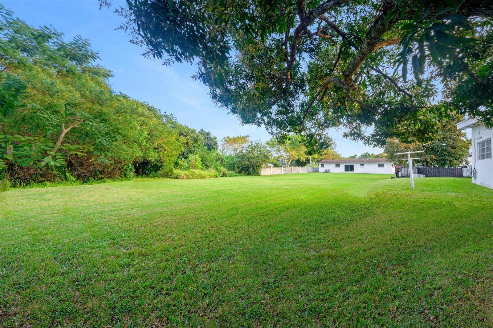 A large, grassy backyard features mature trees, a white house, and a perimeter fence — 13945 N Miami Avenue, Miami FL 33168, MIAMI, FL