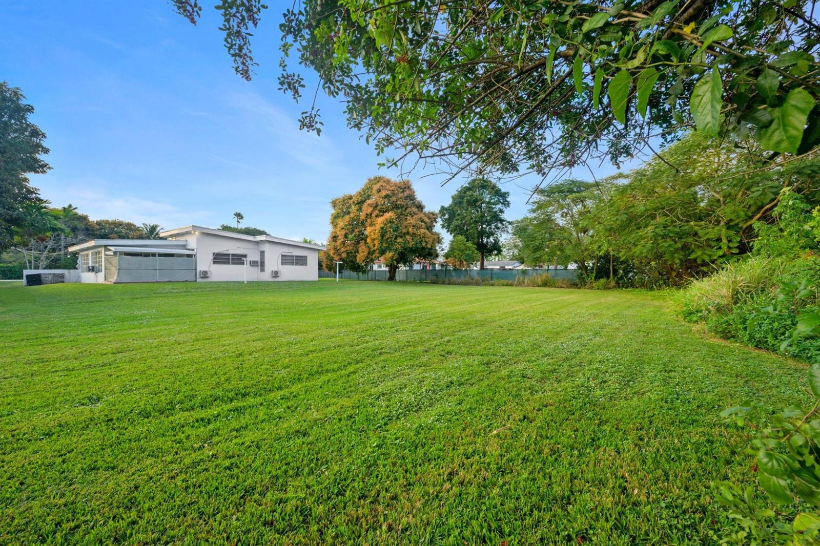 A white house sits at the edge of a large, grassy backyard with mature trees — 13945 N Miami Avenue, Miami FL 33168, MIAMI, FL