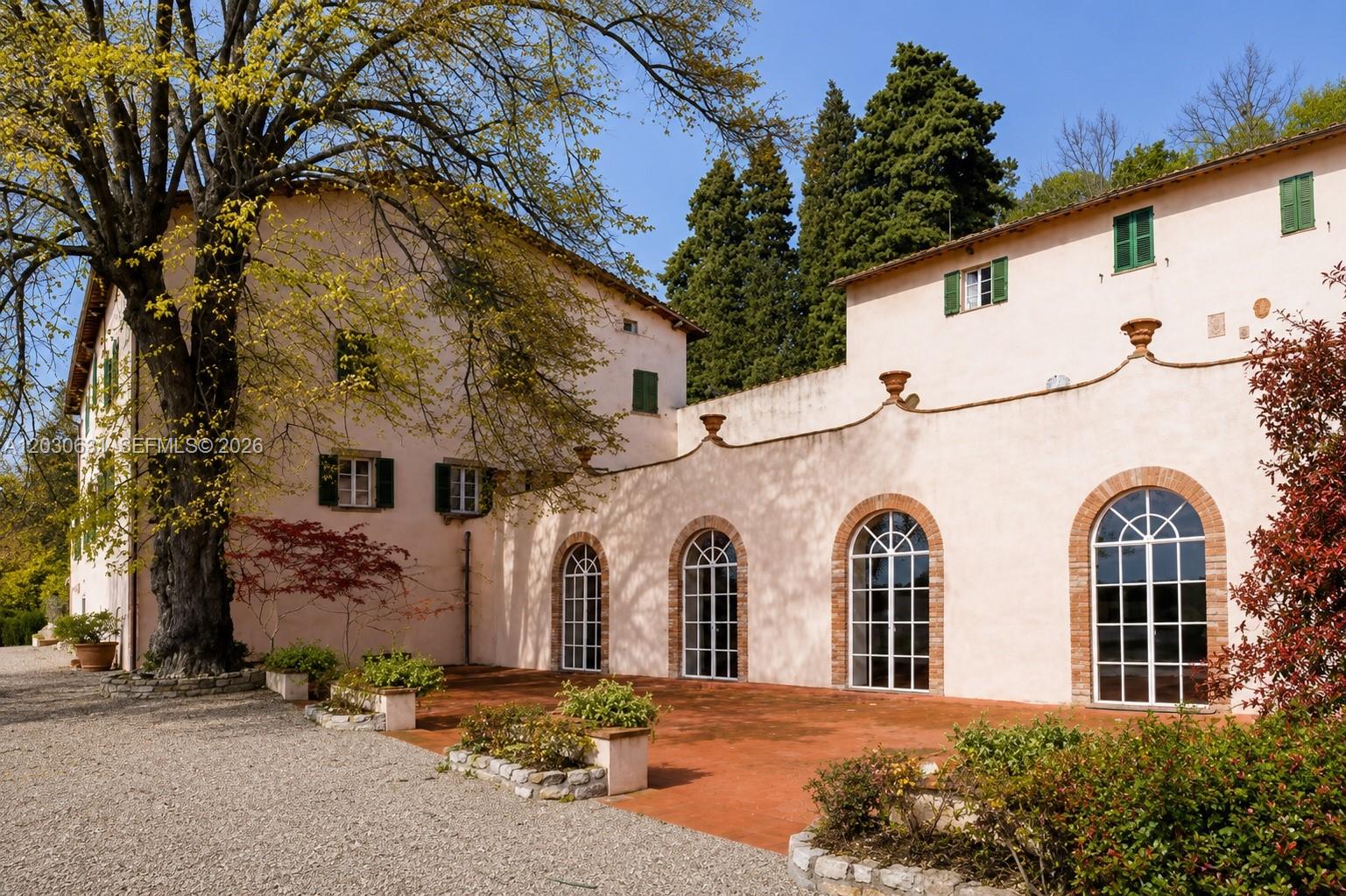 A pale pink villa features arched windows, a terracotta patio, and a large tree — Tuscany Luxury Estate Florence Max Mlekus, FL