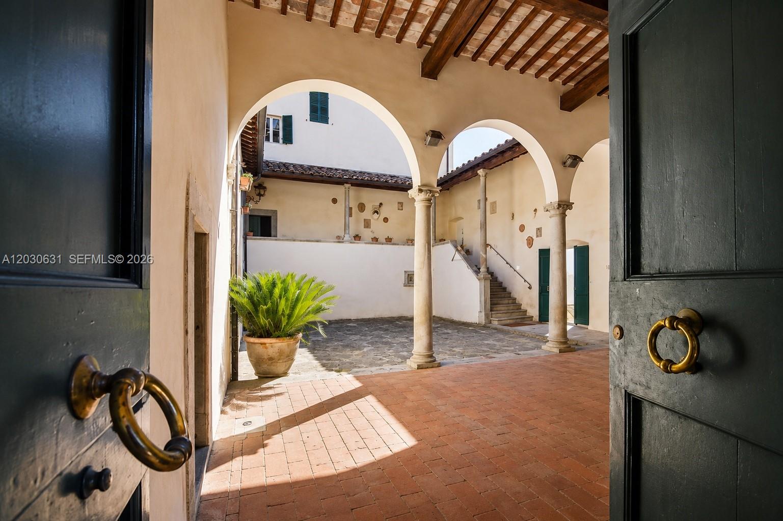 An open doorway reveals a stone-paved courtyard with arched columns, terracotta flooring, and a staircase — Tuscany Luxury Estate Florence Max Mlekus, FL