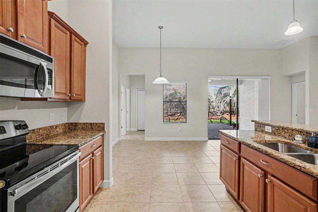 A kitchen with wood cabinets, granite countertops, and tile flooring opens to a dining area — 1392 PALMETTO DUNES STREET, DAVENPORT, FL