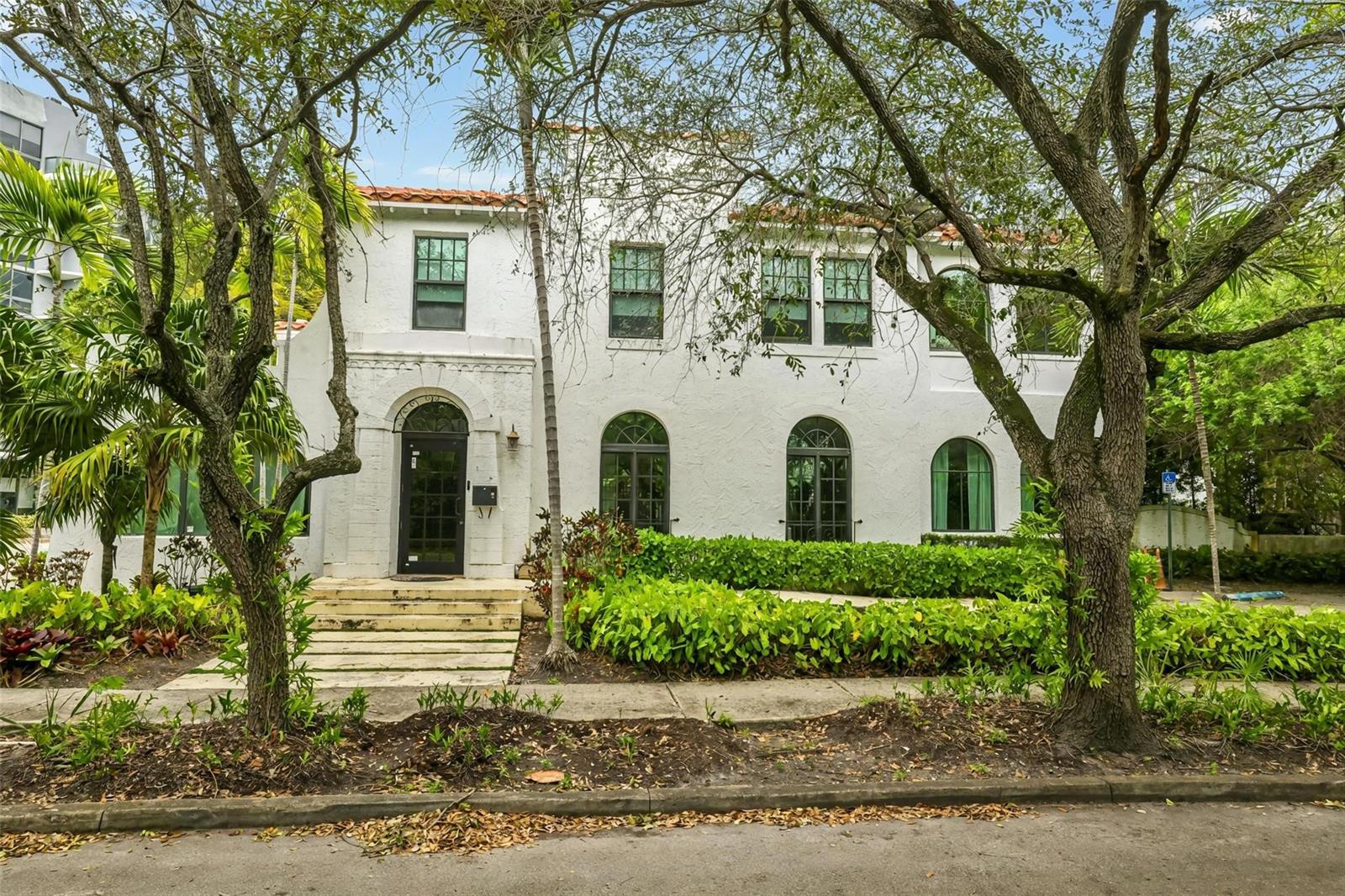 A two-story white stucco building with arched windows and a tiled roof behind large trees — 445 NE 56, Miami FL 33137, MIAMI, FL