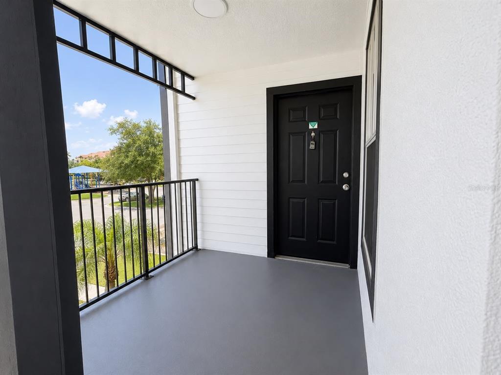 A covered balcony with a black door, metal railing, and a view of a playground — 2217 GRAND CAYMAN COURT UNIT 1223, KISSIMMEE, FL