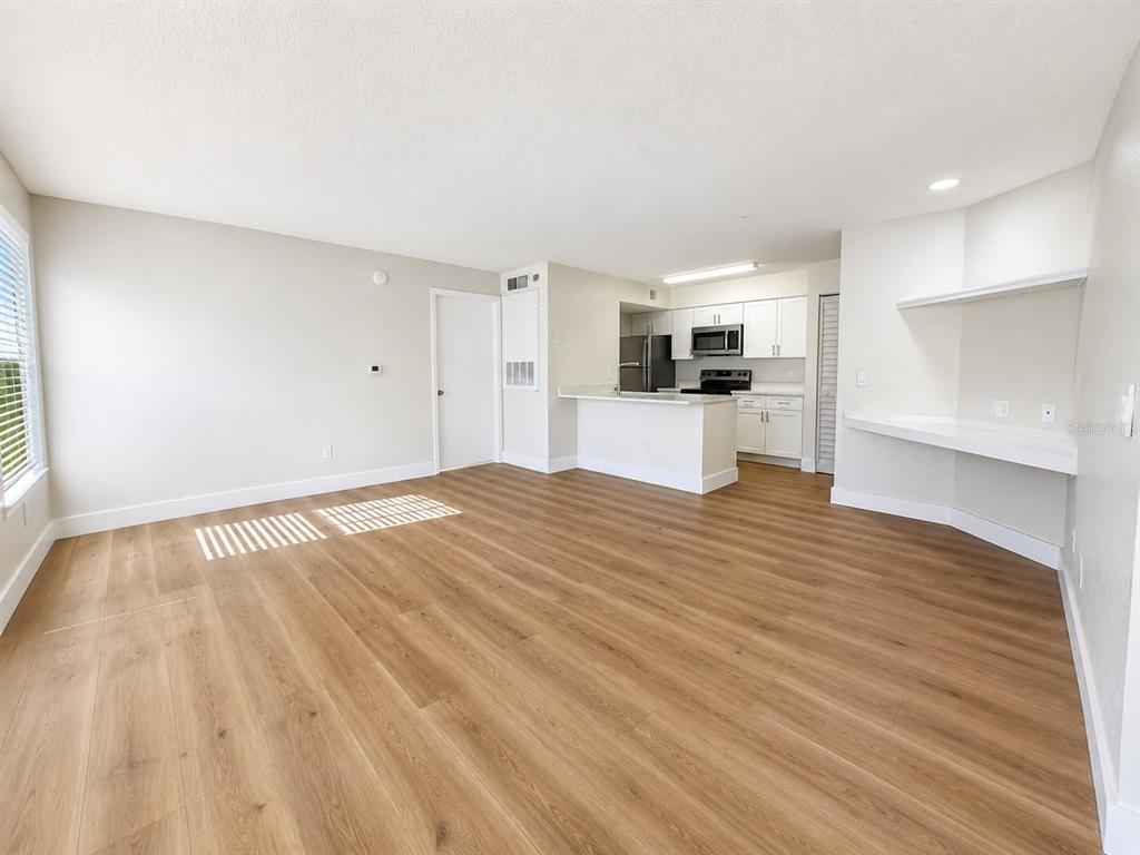 An open-concept living area features light wood-look flooring, white walls, and a kitchen with white cabinets — 2217 GRAND CAYMAN COURT UNIT 1223, KISSIMMEE, FL