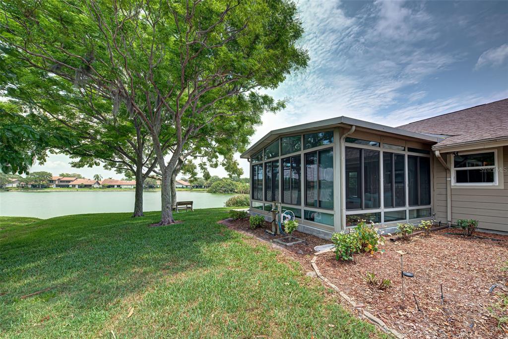 A screened-in porch sits beside a grassy lawn and a lake under a large tree — 3670 EMILY LANE, SARASOTA, FL