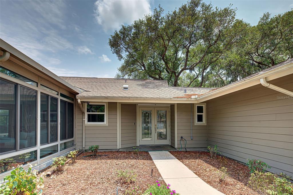 A tan house exterior features a double front door, a concrete walkway, and large trees — 3670 EMILY LANE, SARASOTA, FL
