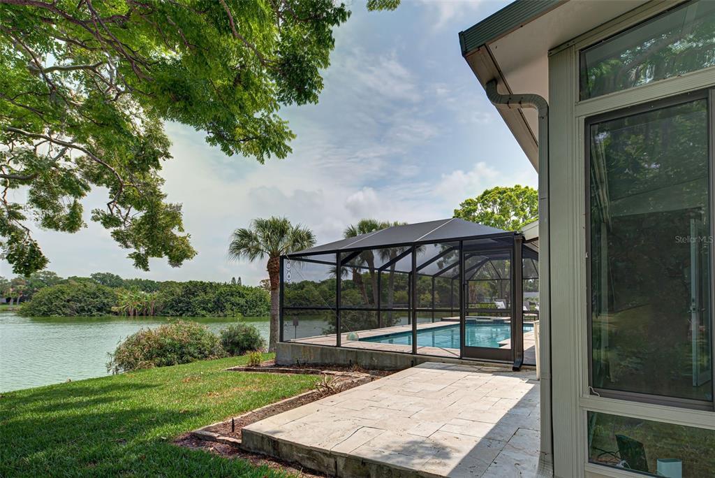 A screened-in pool sits on a patio next to a house overlooking a lake — 3670 EMILY LANE, SARASOTA, FL