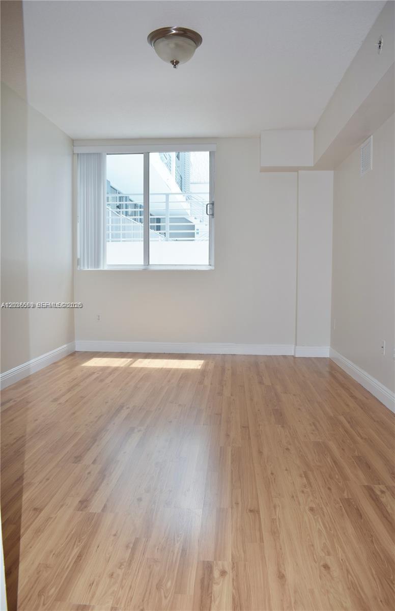 An empty room features light wood-look flooring, beige walls, and a window with blinds — 3339 Virginia St # 207, Miami FL 33133, MIAMI, FL