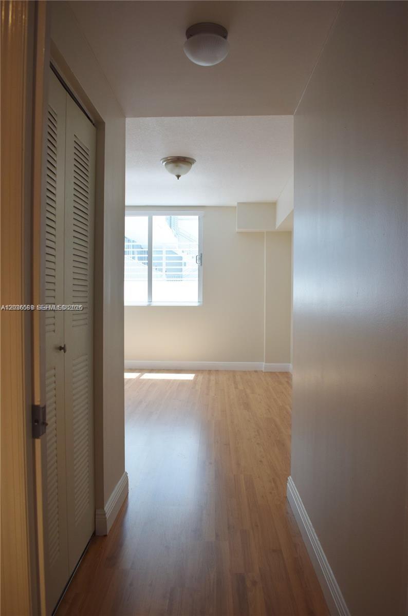 A hallway with light wood flooring leads to a room with a window — 3339 Virginia St # 207, Miami FL 33133, MIAMI, FL