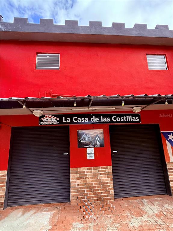 The exterior of a red building features two black roll-down doors and a sign — 149 ROUTE UNIT KM 18.3, CIALES, PR