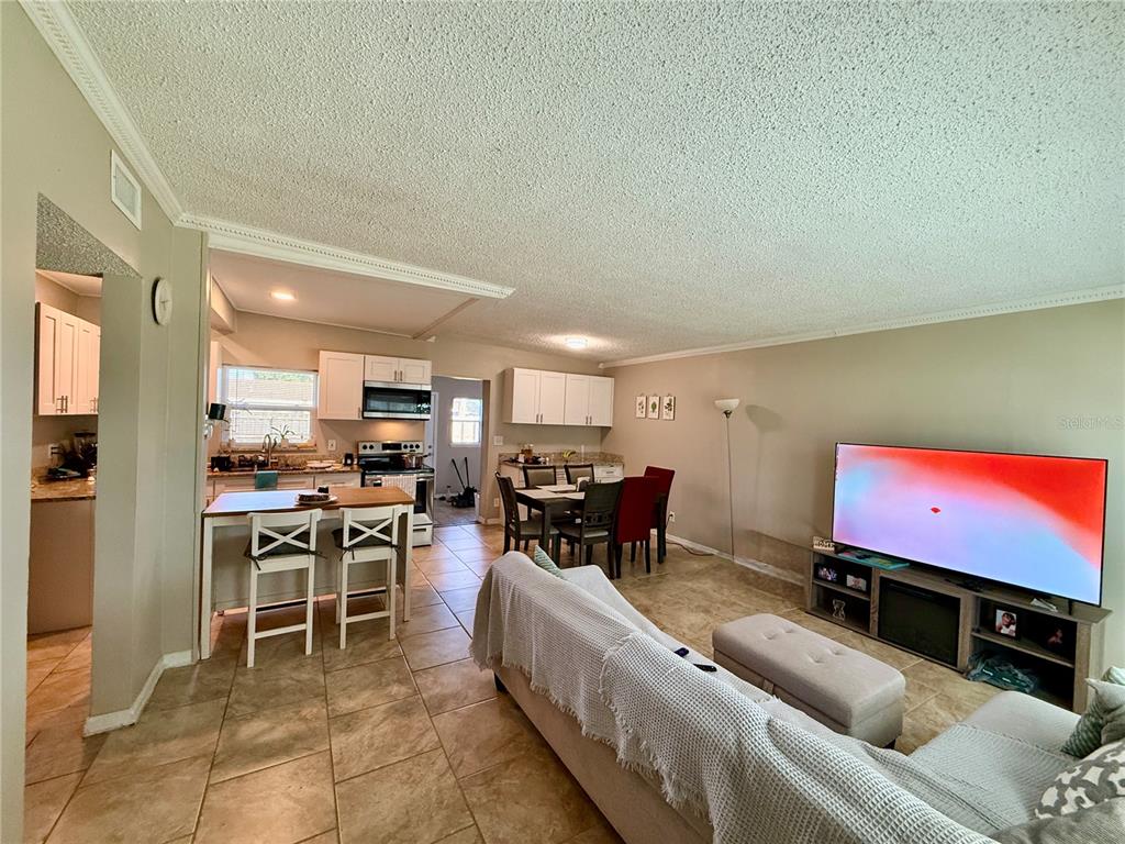 An open-concept living and dining area features tile flooring, white cabinetry, and a large television — 1604 CRYSTAL COURT E, LAKELAND, FL