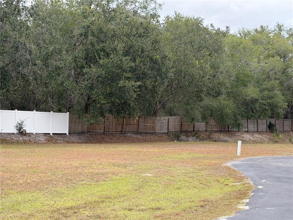 A grassy vacant lot features a white vinyl fence and a wooden fence bordering trees — MONTCLAIR ROAD UNIT 21, LEESBURG, FL