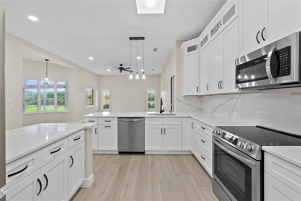 A modern kitchen features white cabinetry, stainless steel appliances, and a marble-patterned backsplash — 38 KINGSLEY CIRCLE, ORMOND BEACH, FL