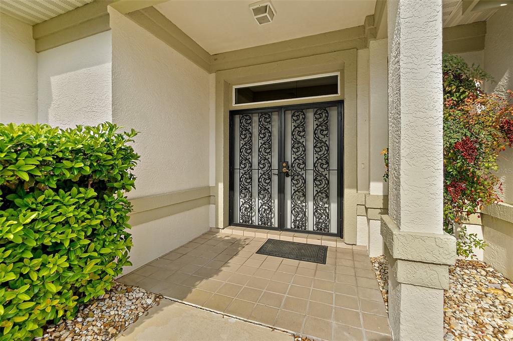 A covered entryway features a tiled porch, a decorative double screen door, and surrounding landscaping — 38 KINGSLEY CIRCLE, ORMOND BEACH, FL