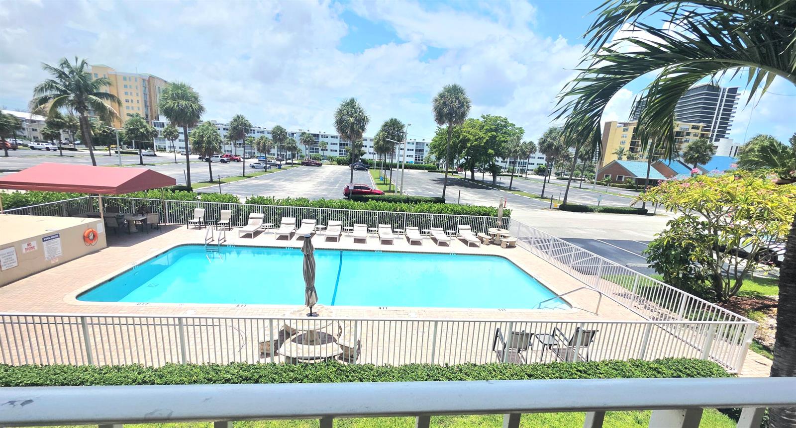 An elevated view of a rectangular swimming pool with lounge chairs and a parking lot — 3200 NE 7th Court # 202b, Pompano Beach FL 33062, POMPANO BEACH, FL