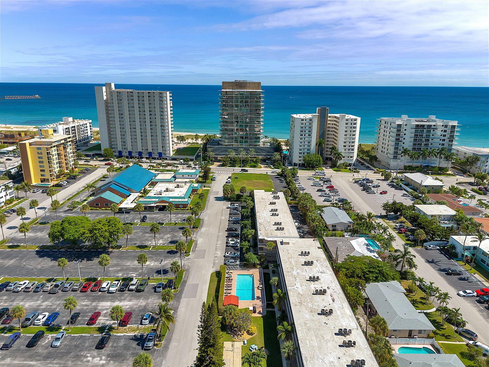 An aerial view shows several high-rise buildings, parking lots, and a swimming pool near the ocean — 3200 NE 7th Court # 202b, Pompano Beach FL 33062, POMPANO BEACH, FL