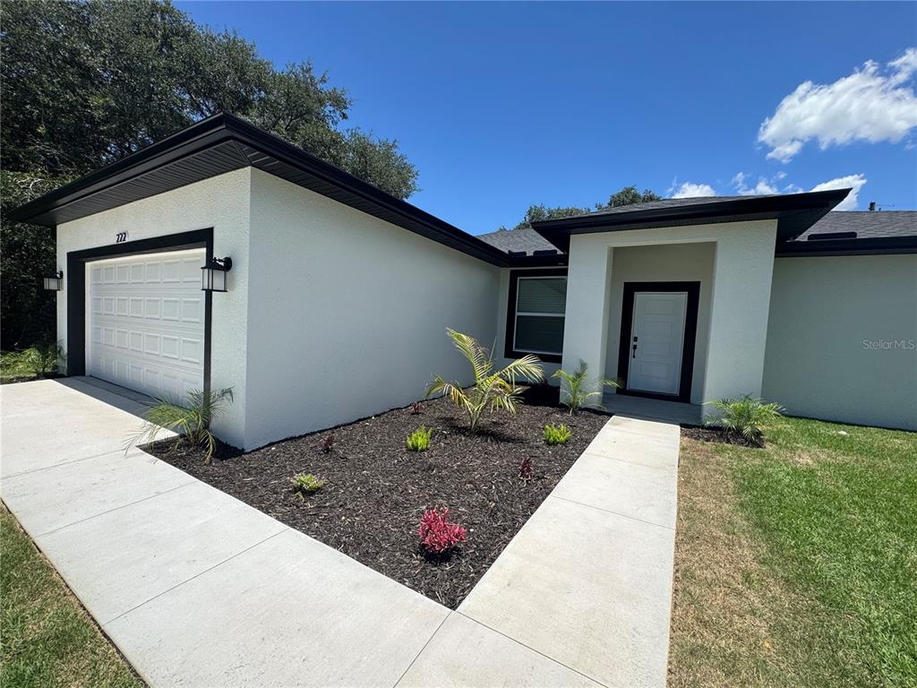 A white house with black trim features a garage, front entrance, and landscaped garden bed — 222 FLORIDA AVENUE, DUNDEE, FL