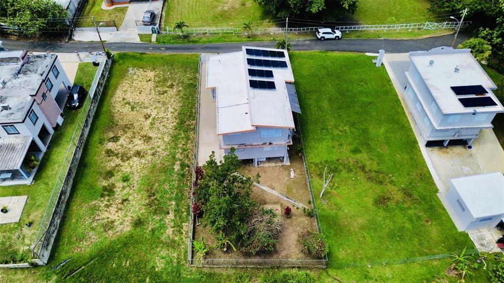 An aerial view shows a two-story house with solar panels on a residential lot — Bo Ceiba Sur Sector Canal SOLAR #6, JUNCOS, PR