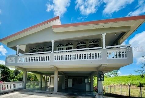 A two-story house with a white balcony railing stands on concrete stilts under a blue sky — Bo Ceiba Sur Sector Canal SOLAR #6, JUNCOS, PR