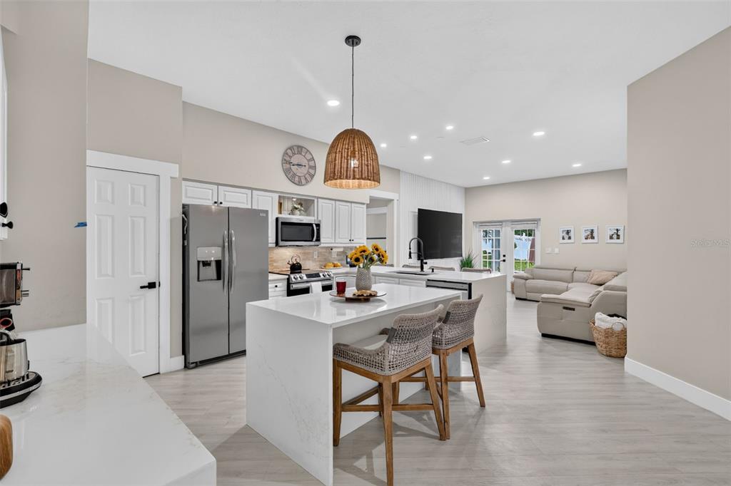 A modern open-concept kitchen features a white quartz island, stainless steel appliances, and light flooring — 33150 KAYLEE WAY, LEESBURG, FL