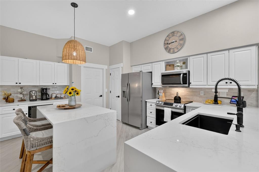 A modern kitchen features white cabinetry, quartz countertops, a center island, and stainless steel appliances — 33150 KAYLEE WAY, LEESBURG, FL