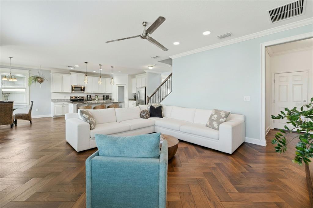 A living room with a white sectional sofa, blue armchair, and herringbone wood flooring — 18799 HENEQUEN LANE SE, SPRING HILL, FL
