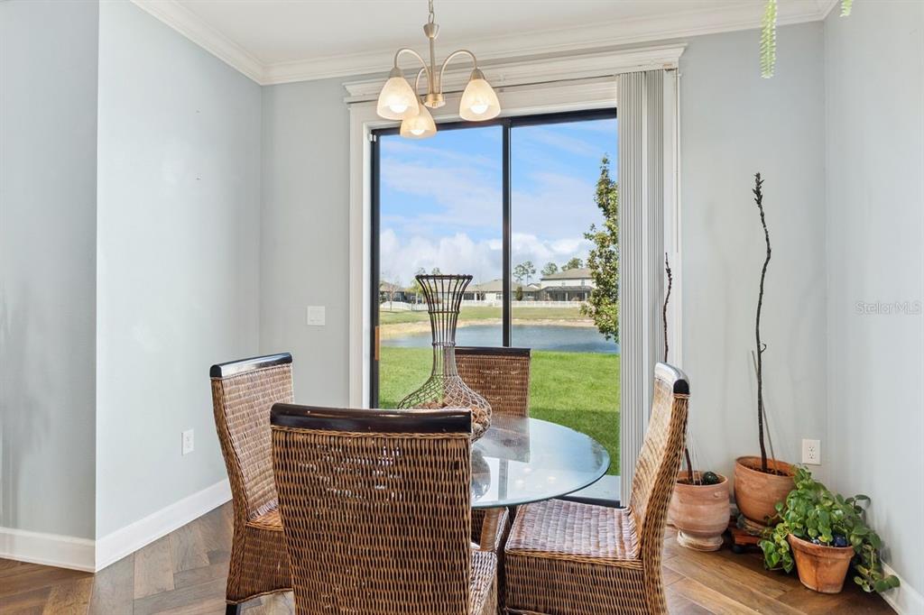 A dining area with a glass table, wicker chairs, and sliding doors overlooking a pond — 18799 HENEQUEN LANE SE, SPRING HILL, FL