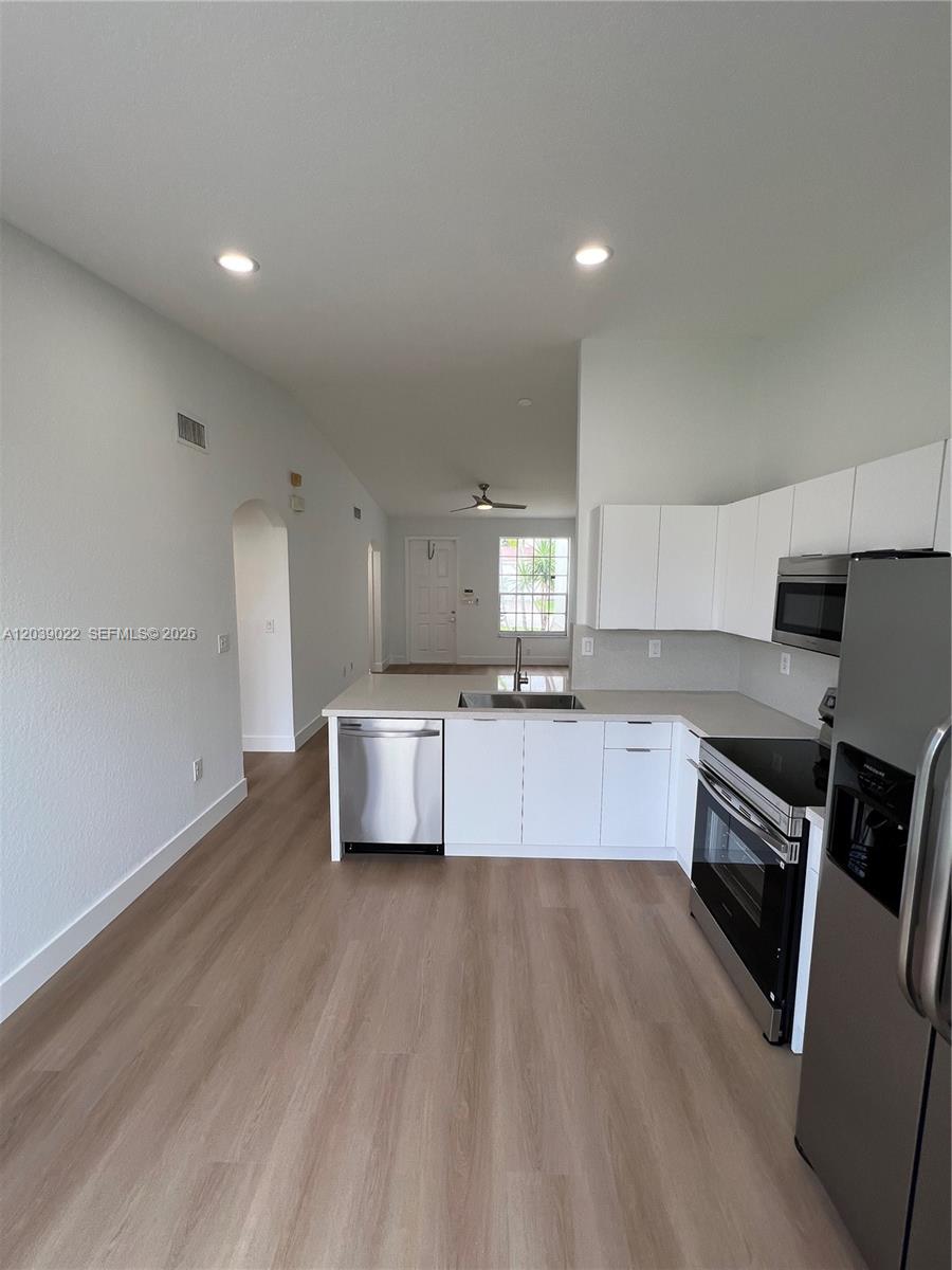 A modern kitchen with white cabinets and stainless steel appliances opens into a living area — 18739 SW 28th St, Miramar FL 33029, MIRAMAR, FL