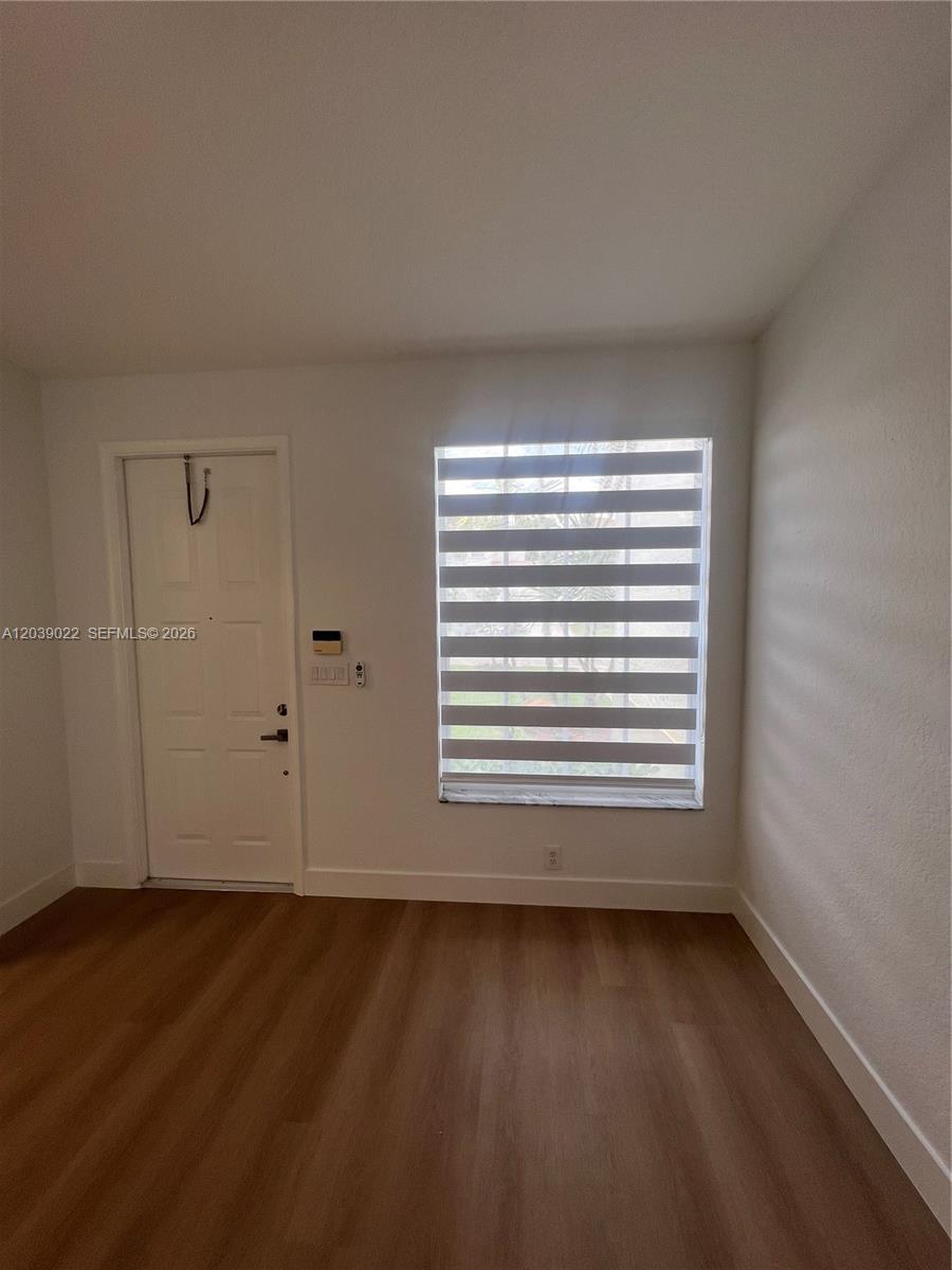 An empty room features white walls, light wood-look flooring, and a window with striped blinds — 18739 SW 28th St, Miramar FL 33029, MIRAMAR, FL