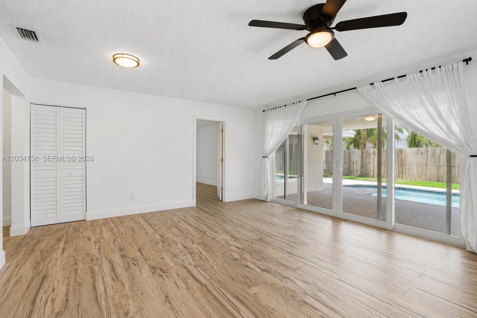 An empty room features wood-look flooring, a ceiling fan, and sliding glass doors to a pool — 5874 SW 97th Ter, Cooper City FL 33328, COOPER CITY, FL