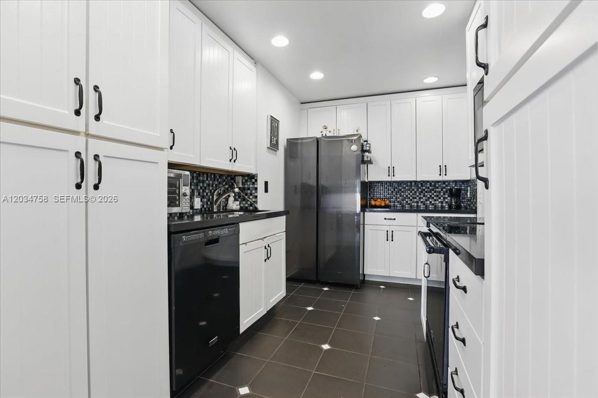 A galley-style kitchen features white cabinetry, black countertops, stainless steel appliances, and dark tile flooring — 5874 SW 97th Ter, Cooper City FL 33328, COOPER CITY, FL