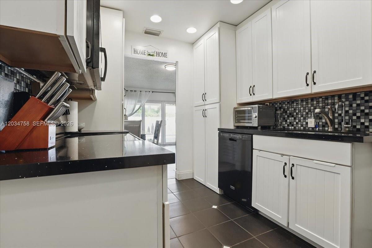 A kitchen features white cabinets, black countertops, a tiled backsplash, and dark floor tiles — 5874 SW 97th Ter, Cooper City FL 33328, COOPER CITY, FL