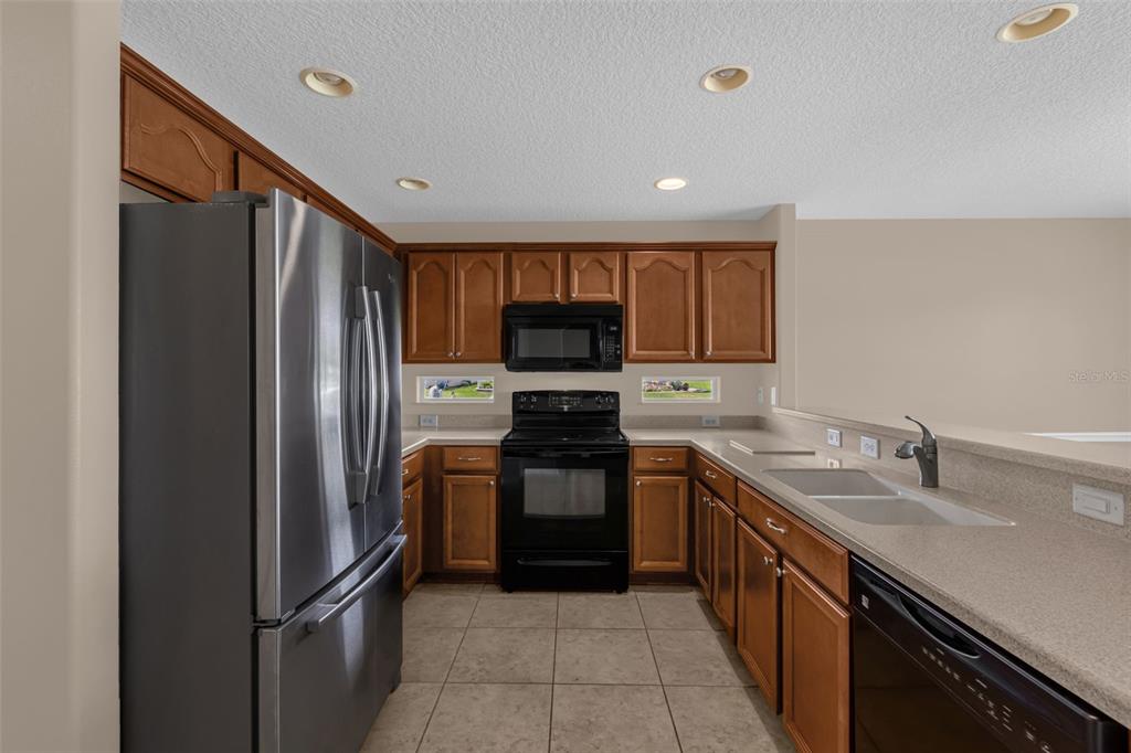 A kitchen features wood cabinets, stainless steel appliances, tile flooring, and a breakfast bar — 5901 CANDLE GLOW PLACE, LEESBURG, FL