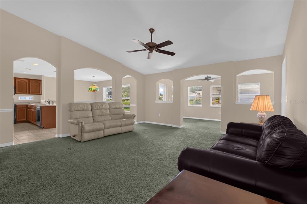 A living room with green carpet, a tan sofa, a black leather sofa, and arched doorways — 5901 CANDLE GLOW PLACE, LEESBURG, FL