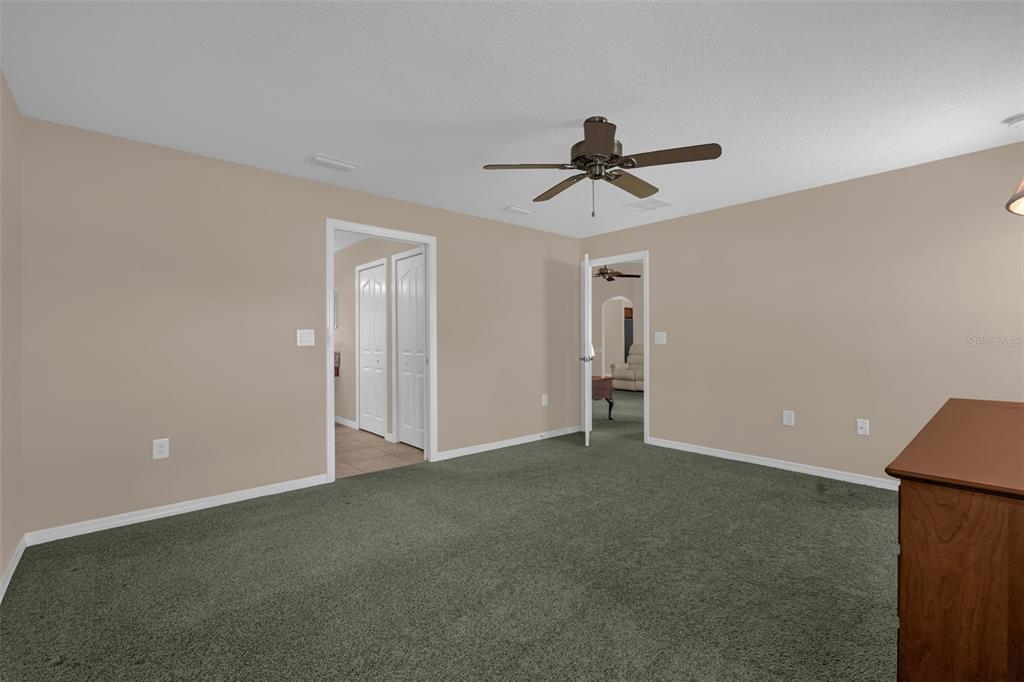 A bedroom with beige walls, green carpeting, a ceiling fan, and two open doorways — 5901 CANDLE GLOW PLACE, LEESBURG, FL
