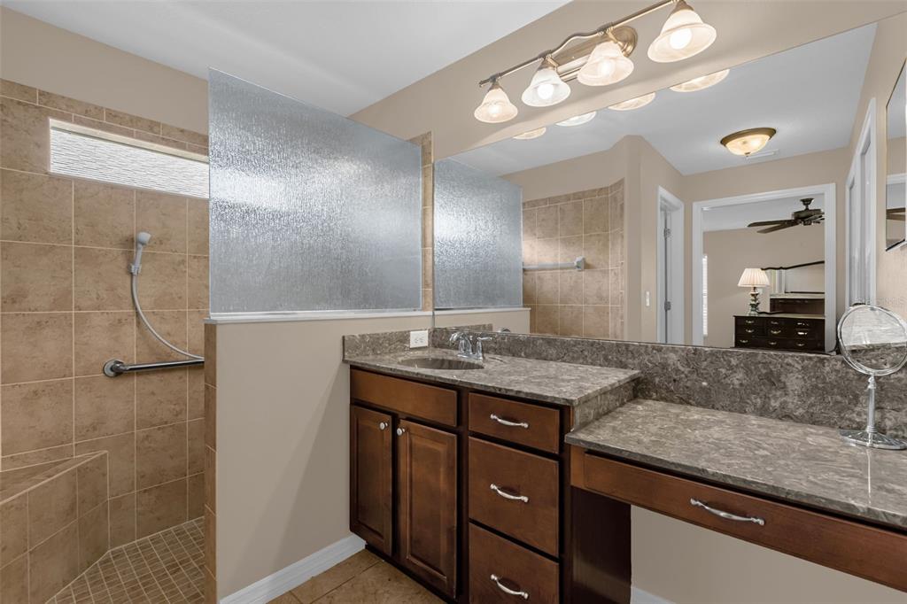 A bathroom features a tiled walk-in shower, a dark wood vanity, and a large mirror — 5901 CANDLE GLOW PLACE, LEESBURG, FL