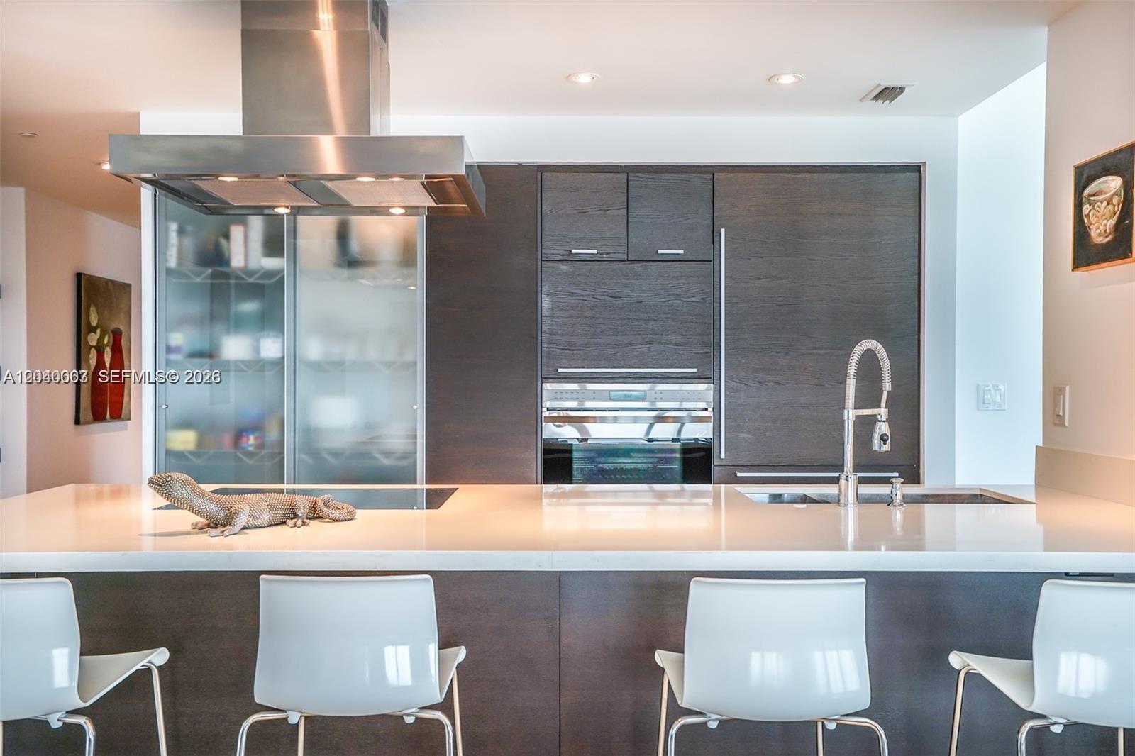 A modern kitchen features dark wood cabinetry, a white island countertop, and stainless steel appliances — 1445 16th St # 1103, Miami Beach FL 33139, MIAMI BEACH, FL