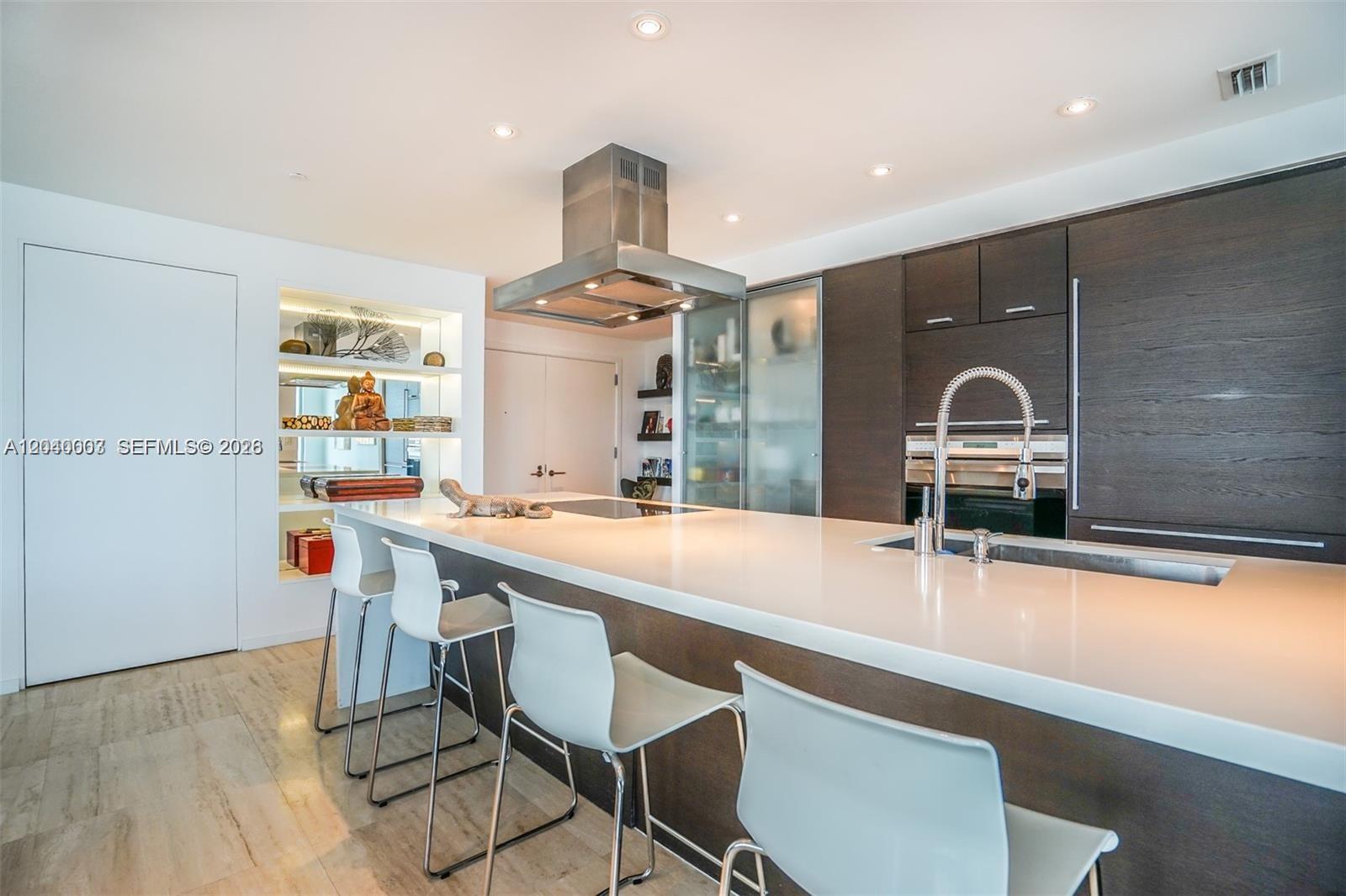 A modern kitchen features dark wood cabinetry, a large white island, and bar stool seating — 1445 16th St # 1103, Miami Beach FL 33139, MIAMI BEACH, FL