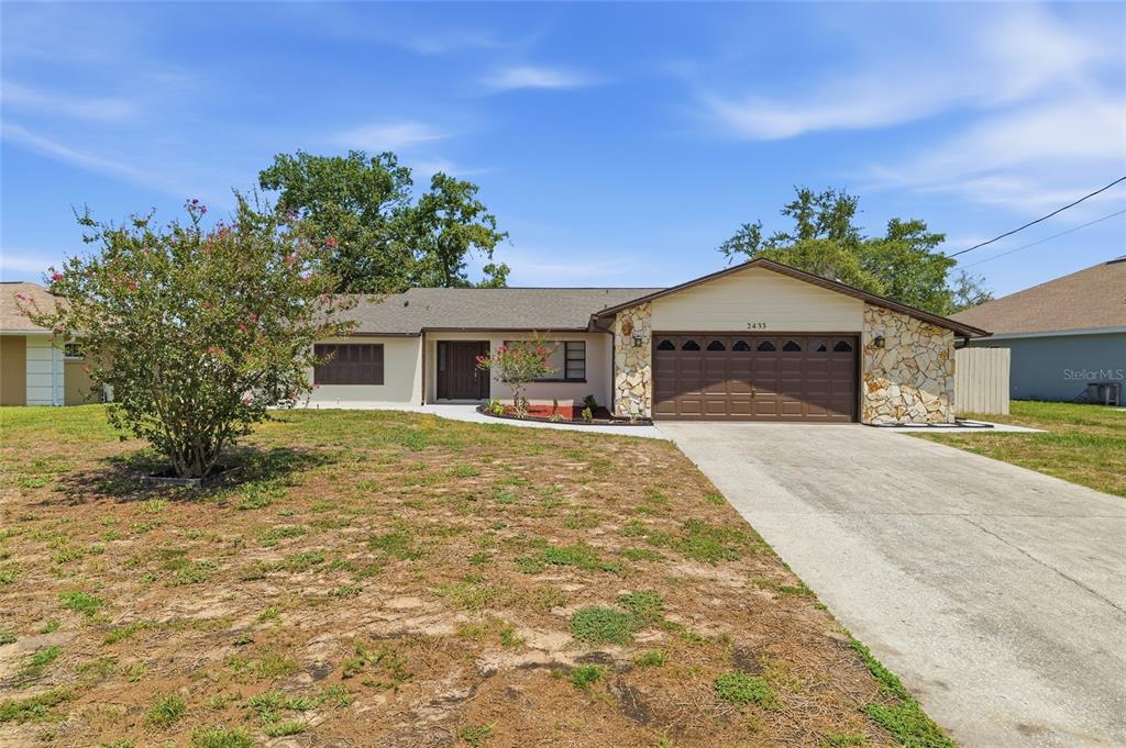 A single-story house with a stone-accented facade, a brown garage door, and a concrete driveway — 2433 WATERFALL DRIVE, SPRING HILL, FL