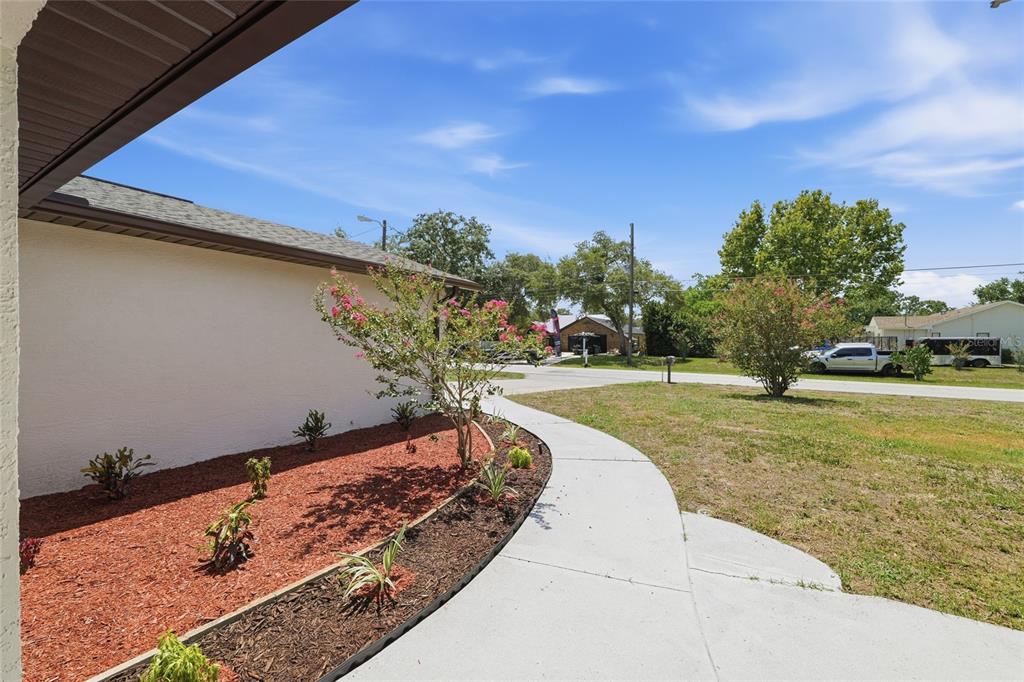 A concrete walkway curves past a landscaped garden bed along the side of a house — 2433 WATERFALL DRIVE, SPRING HILL, FL