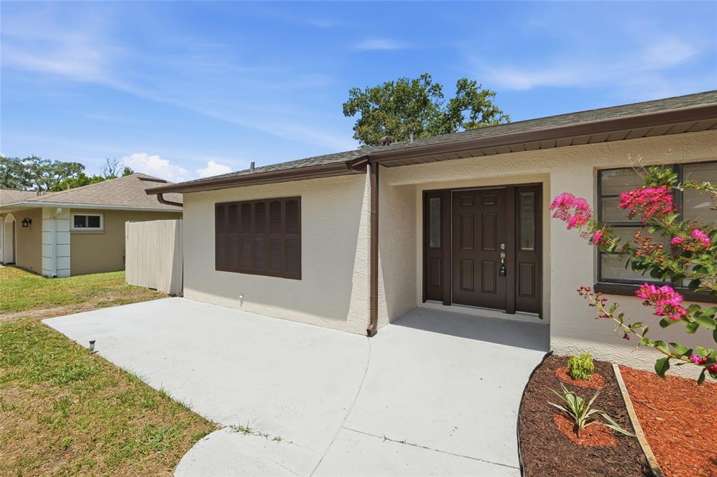 The exterior of a house features a concrete patio, a brown front door, and shutters — 2433 WATERFALL DRIVE, SPRING HILL, FL