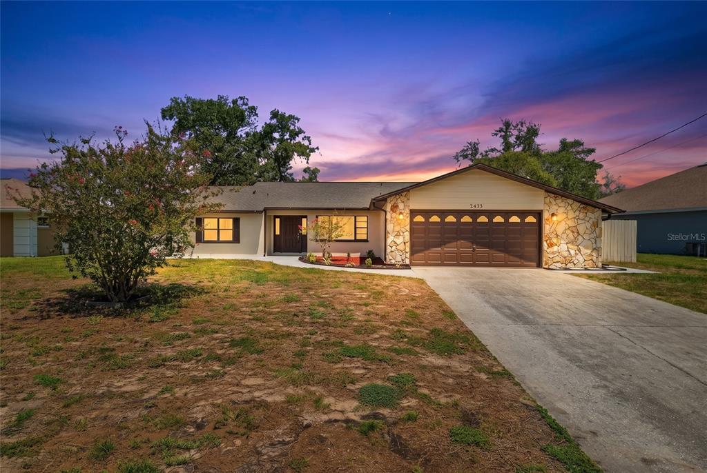 A single-story house with a stone-accented garage and a concrete driveway at sunset — 2433 WATERFALL DRIVE, SPRING HILL, FL