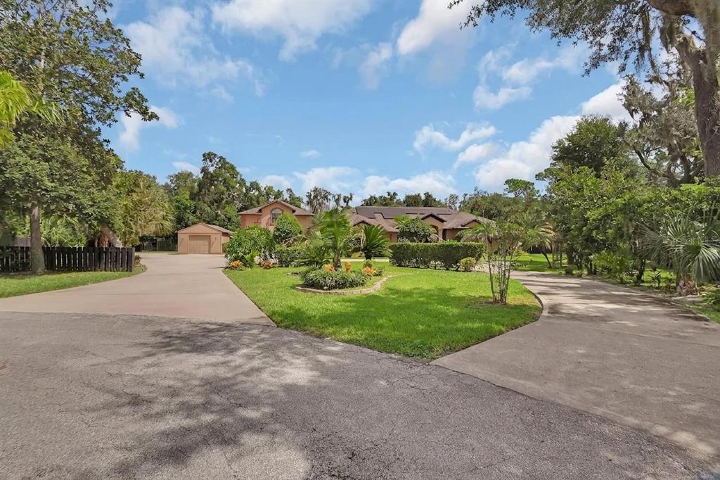 A house with a large lawn, two driveways, and a detached garage under a blue sky — 6241 PALOMINO CIRCLE, PORT ORANGE, FL